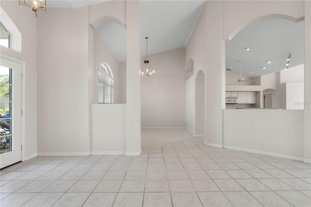 tiled entryway featuring ceiling fan with notable chandelier and high vaulted ceiling