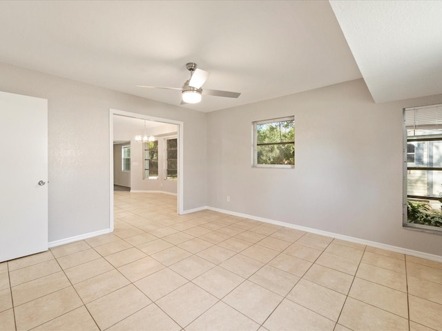 tiled spare room featuring ceiling fan with notable chandelier