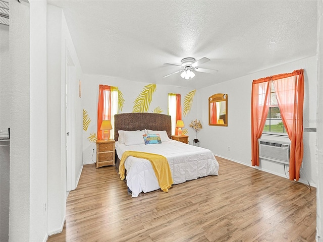 bedroom featuring a textured ceiling, a wall mounted air conditioner, ceiling fan, and light wood-type flooring