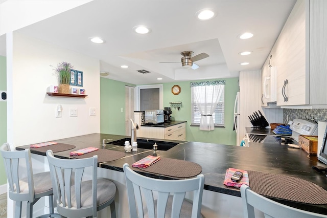 kitchen with a tray ceiling, kitchen peninsula, sink, and range