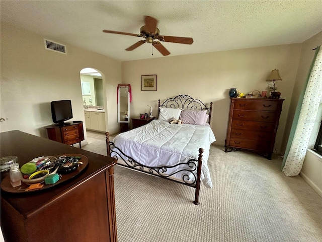 bedroom featuring connected bathroom, ceiling fan, light carpet, and a textured ceiling