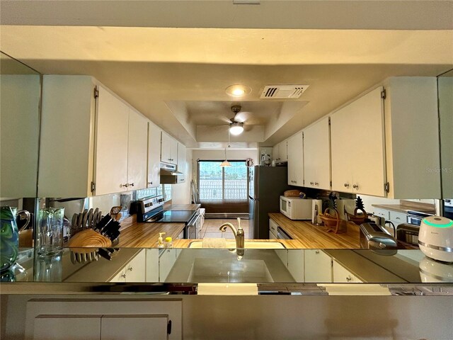 kitchen featuring ceiling fan, a raised ceiling, white cabinetry, and appliances with stainless steel finishes