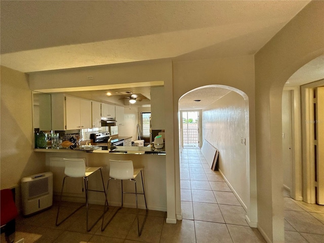 kitchen with kitchen peninsula, stainless steel electric range oven, ceiling fan, light tile patterned floors, and white cabinetry