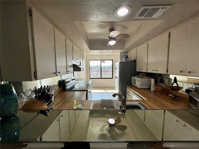 kitchen with a raised ceiling, sink, ceiling fan, butcher block countertops, and range