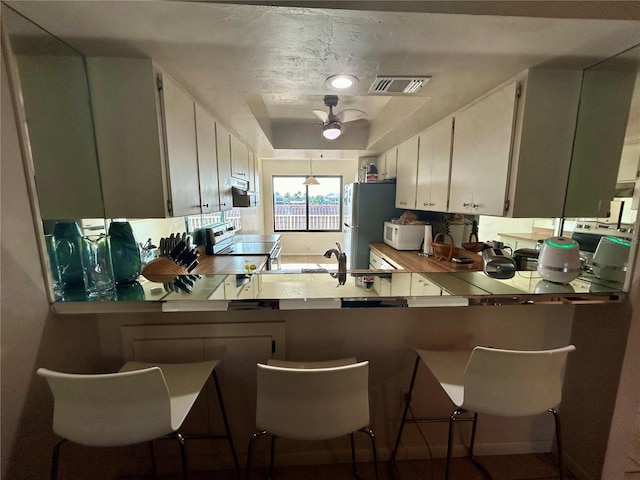 kitchen with a breakfast bar, white cabinetry, white appliances, and kitchen peninsula