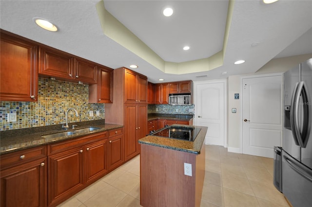 kitchen with sink, a kitchen island, dark stone countertops, appliances with stainless steel finishes, and a tray ceiling