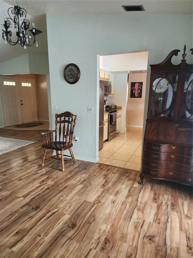 hallway featuring an inviting chandelier, lofted ceiling, and light tile floors