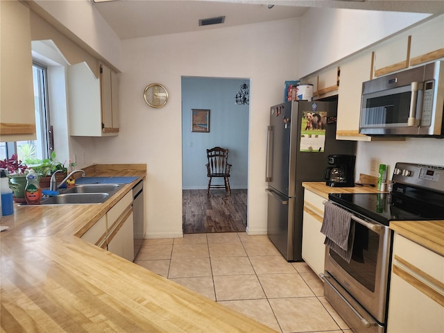 kitchen featuring wood counters, vaulted ceiling, appliances with stainless steel finishes, and light tile floors