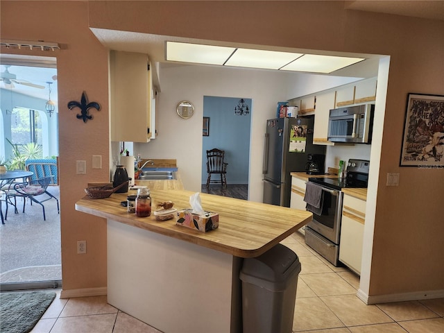 kitchen featuring kitchen peninsula, ceiling fan, light tile flooring, appliances with stainless steel finishes, and sink