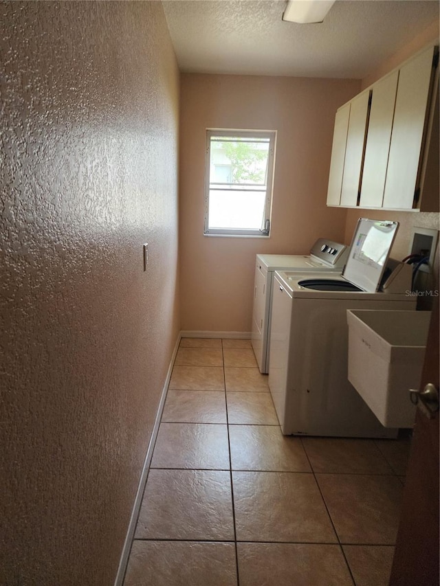 clothes washing area featuring light tile floors, washer and clothes dryer, cabinets, and sink