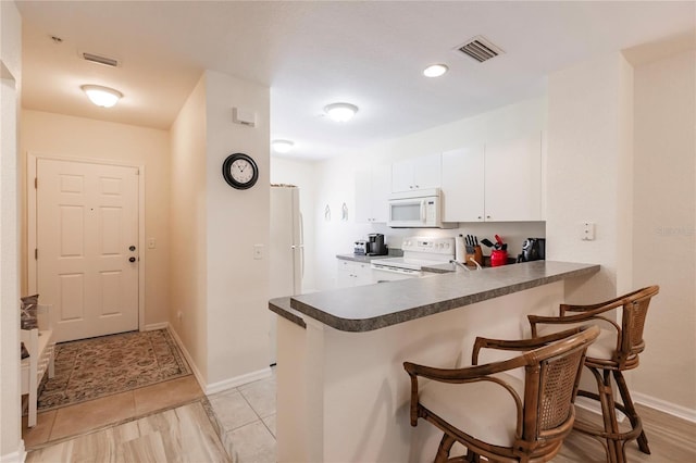 kitchen with kitchen peninsula, white cabinets, a breakfast bar area, and white appliances