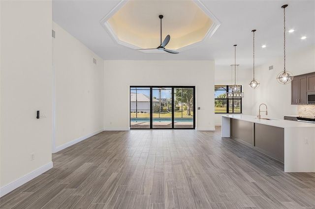 kitchen with ceiling fan, sink, backsplash, a raised ceiling, and hanging light fixtures