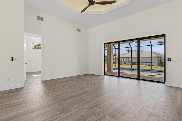 empty room featuring a raised ceiling, ceiling fan, and light wood-type flooring