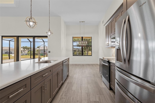 kitchen featuring a notable chandelier, appliances with stainless steel finishes, light hardwood / wood-style flooring, sink, and pendant lighting