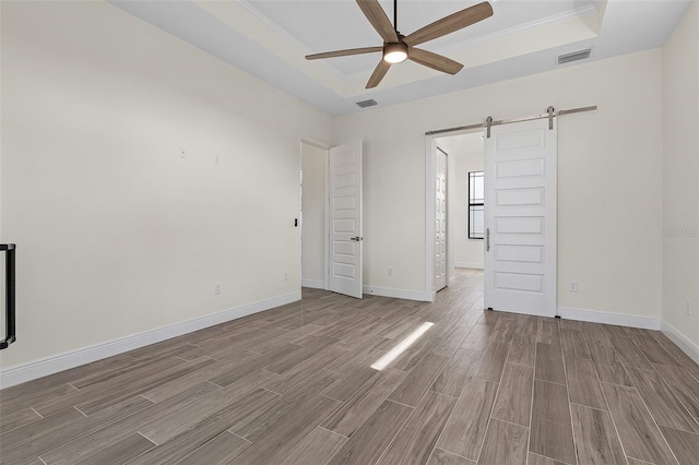 interior space featuring hardwood / wood-style floors, ornamental molding, a barn door, a raised ceiling, and ceiling fan