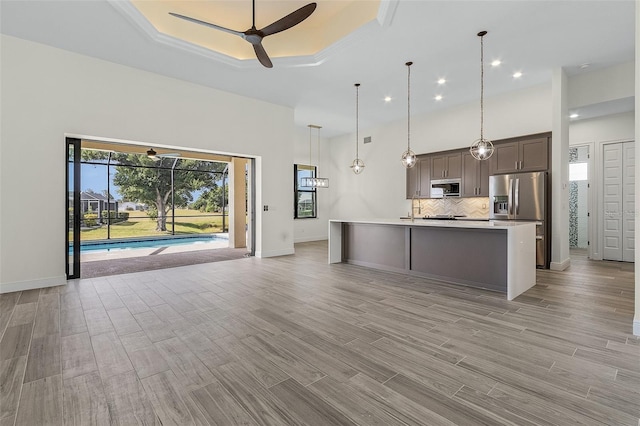 kitchen with pendant lighting, backsplash, stainless steel appliances, ceiling fan, and an island with sink