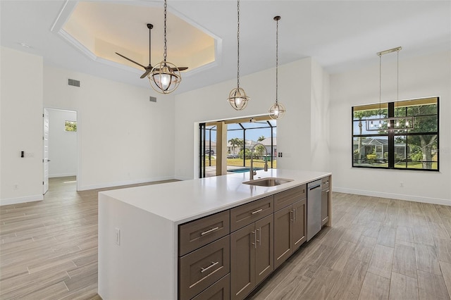 kitchen with hanging light fixtures, an island with sink, light hardwood / wood-style floors, and a tray ceiling