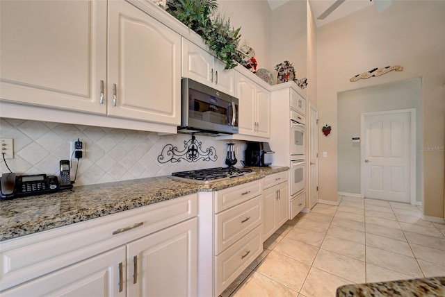 kitchen with decorative backsplash, appliances with stainless steel finishes, light stone counters, white cabinets, and light tile patterned flooring