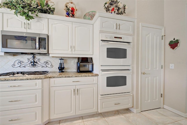 kitchen with decorative backsplash, appliances with stainless steel finishes, light stone counters, white cabinetry, and light tile patterned flooring