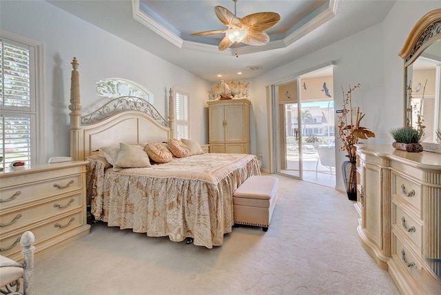 carpeted bedroom with access to exterior, multiple windows, a tray ceiling, and ceiling fan