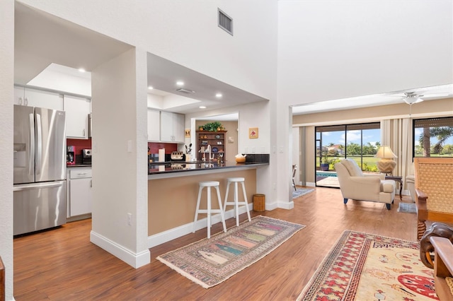 kitchen featuring kitchen peninsula, ceiling fan, stainless steel fridge, light hardwood / wood-style floors, and white cabinets