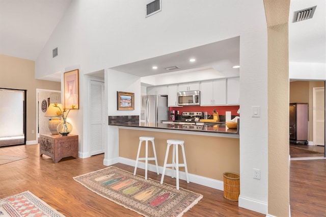 kitchen featuring appliances with stainless steel finishes, hardwood / wood-style floors, a kitchen breakfast bar, and white cabinetry