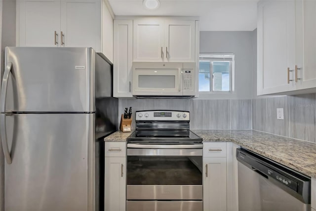 kitchen featuring appliances with stainless steel finishes, decorative backsplash, white cabinets, and light stone counters