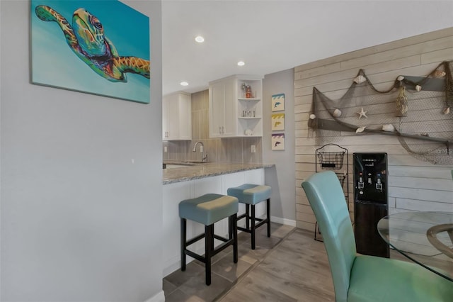 kitchen featuring open shelves, light stone counters, a sink, tasteful backsplash, and a breakfast bar area