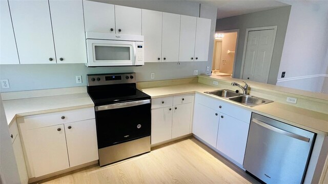 kitchen with kitchen peninsula, appliances with stainless steel finishes, sink, light hardwood / wood-style flooring, and white cabinets