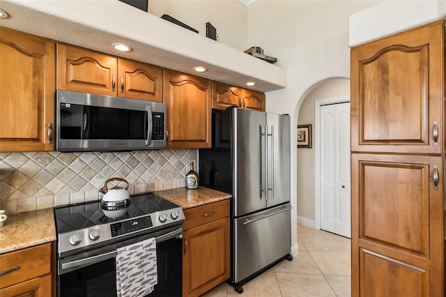 kitchen with light tile flooring, light stone countertops, tasteful backsplash, and stainless steel appliances