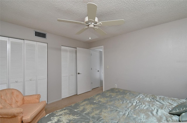 bedroom featuring a textured ceiling, two closets, ceiling fan, and light colored carpet