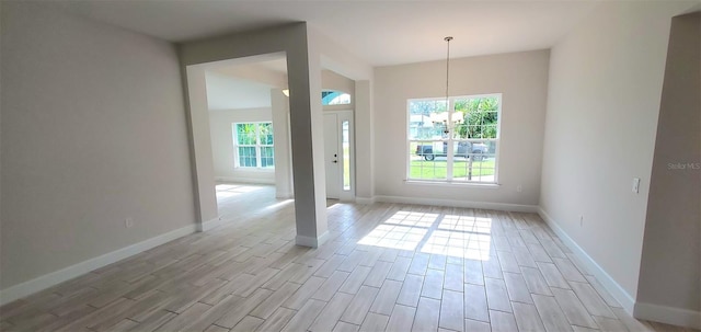 empty room featuring light wood-type flooring, a chandelier, and plenty of natural light