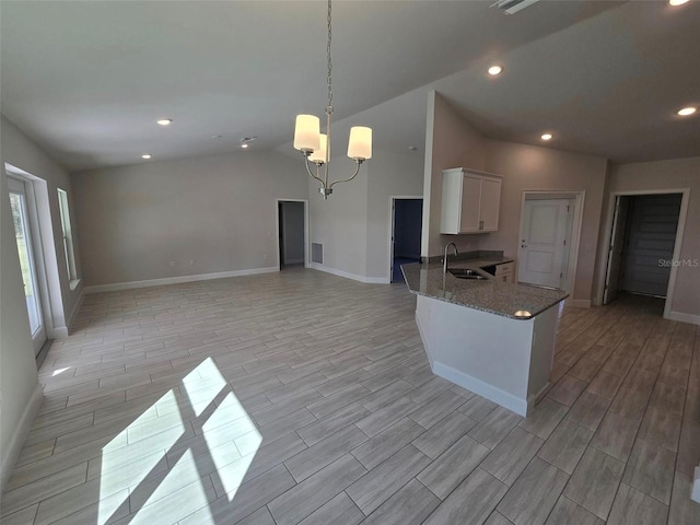 kitchen featuring wood finish floors, decorative light fixtures, white cabinetry, a sink, and dark stone countertops