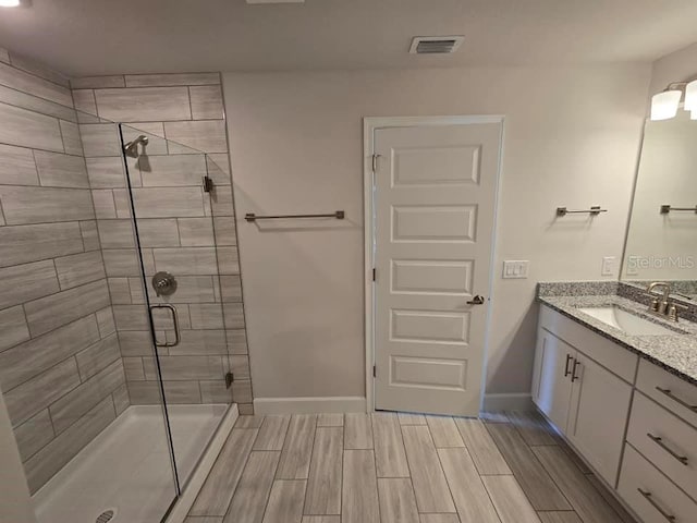 bathroom featuring wood finish floors, visible vents, a shower stall, vanity, and baseboards