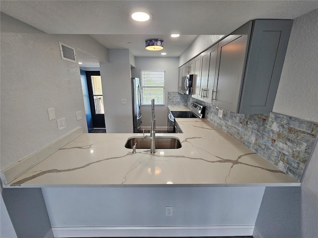 kitchen featuring appliances with stainless steel finishes, light stone counters, gray cabinetry, and tasteful backsplash