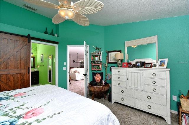 bedroom with ceiling fan, a barn door, a textured ceiling, dark carpet, and ensuite bathroom