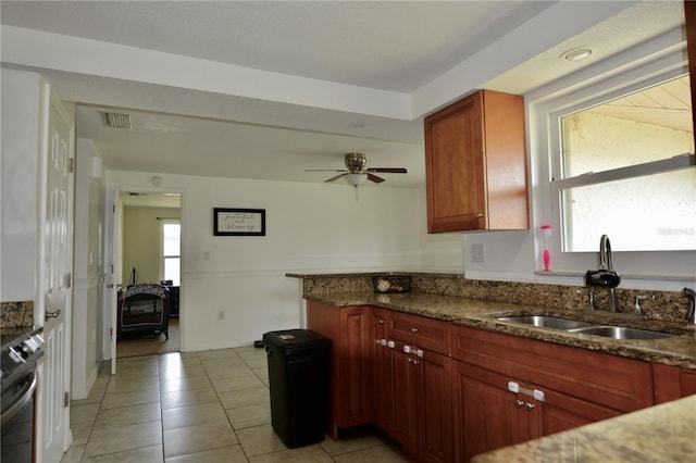 kitchen featuring ceiling fan, dark stone countertops, a wood stove, and plenty of natural light