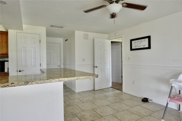 kitchen featuring a textured ceiling, ceiling fan, light tile floors, and light stone countertops