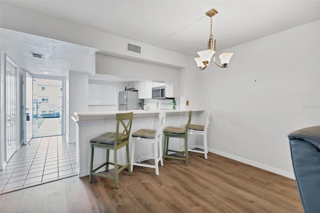 kitchen featuring white refrigerator, kitchen peninsula, hardwood / wood-style floors, a breakfast bar area, and white cabinets