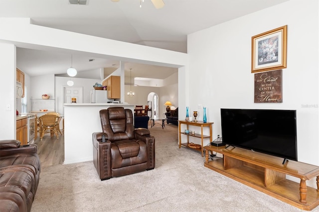 carpeted living room featuring ceiling fan with notable chandelier and vaulted ceiling