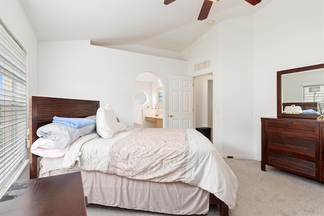 carpeted bedroom with ensuite bathroom, multiple windows, vaulted ceiling, and ceiling fan