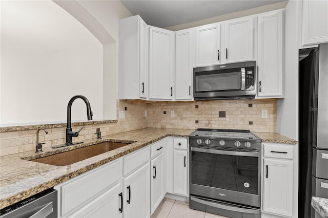 kitchen with sink, light tile patterned floors, appliances with stainless steel finishes, light stone counters, and white cabinetry