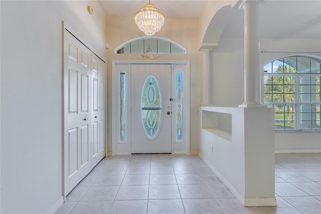 foyer with an inviting chandelier, a high ceiling, decorative columns, and light tile floors