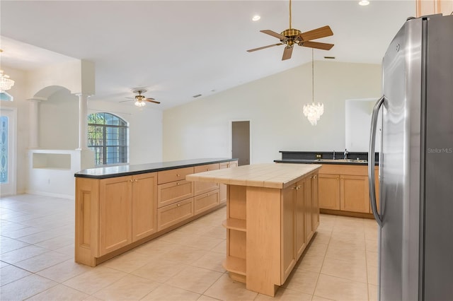 kitchen with ceiling fan with notable chandelier, light tile flooring, a center island, tile counters, and stainless steel refrigerator