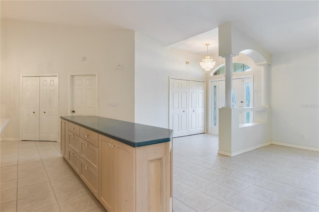 kitchen with light tile flooring, an inviting chandelier, light brown cabinets, high vaulted ceiling, and pendant lighting