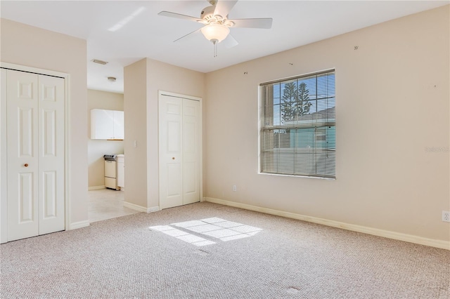 unfurnished bedroom with ceiling fan, two closets, and light colored carpet