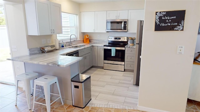 kitchen with appliances with stainless steel finishes, light tile floors, sink, kitchen peninsula, and white cabinetry