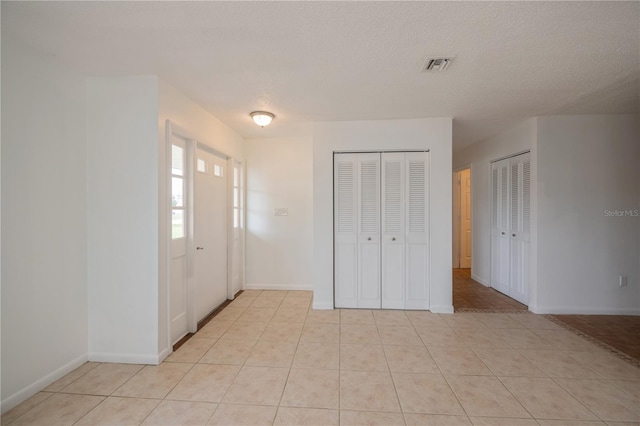 unfurnished bedroom featuring light tile patterned floors, a textured ceiling, and two closets