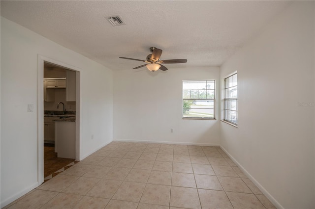 empty room featuring ceiling fan, sink, light tile patterned floors, and a textured ceiling