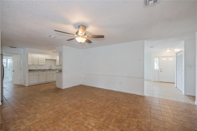 unfurnished living room with ceiling fan, sink, light tile patterned floors, and a textured ceiling